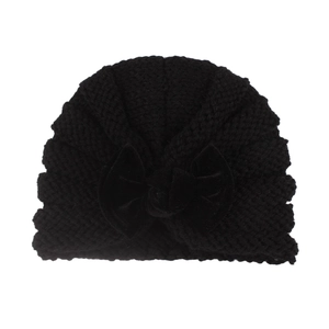 Detail of baby winter knit turban hat featuring a large black velvet bow on white background