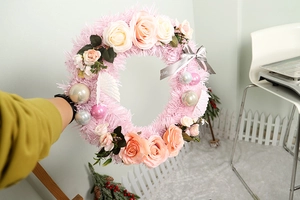 Detail of pink Christmas wreath featuring artificial roses, silver baubles and feathers
