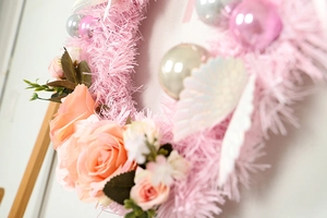Close-up of pink Christmas wreath with silk roses, glitter wings and metallic baubles