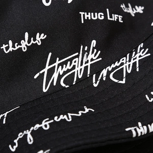 Dettaglio cappello bucket in tela nera con ricamo Thug Life bianco e stile hip-hop urbano
