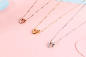 Three hollow heart pendants in rose gold, gold, and silver with small crystals