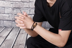 Detail of multi-layer black leather bracelet with golden key pendant on male wrist