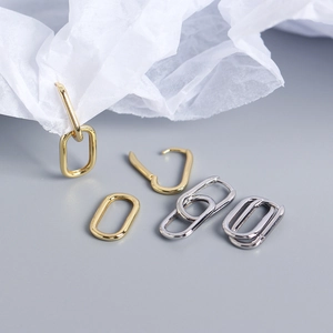 Detail view of gold and silver minimalist oval paperclip hoop earrings on white paper