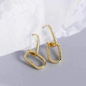 Macro shot of interlocking oval gold earrings on white textured paper background