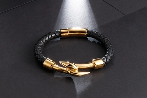 Detail of men's black braided leather bracelet with golden hook-shaped metal buckle