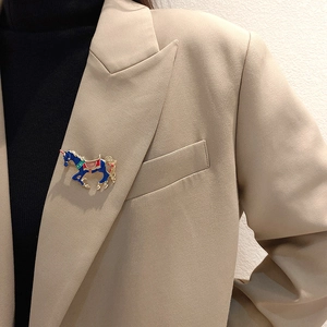 Detailed view of an enamel horse brooch in blue and red on a beige suit lapel
