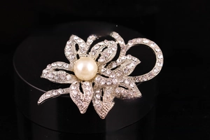 Close-up of silver flower brooch featuring a large pearl and sparkling rhinestones