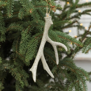Silver glitter reindeer antler ornament hanging on a Christmas tree with festive lights