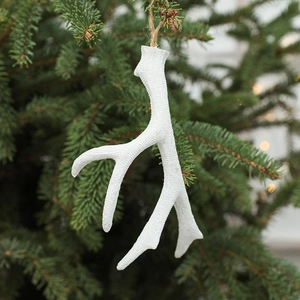 White reindeer antler ornament on Christmas tree branch with festive warm bokeh background