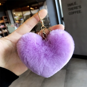 Close-up of fluffy purple heart keychain with gold clasp held against a cafe background