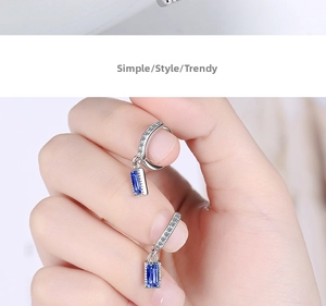 Detailed macro view of silver hoop earrings with rectangular blue zircon pendants