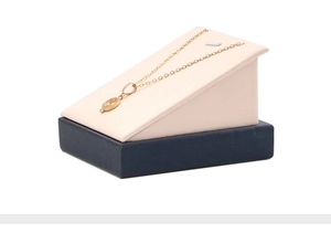 Detail of a gold oval necklace with clear stone on pink and navy blue display stand