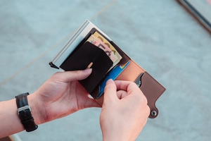 Detailed view of hands inserting credit card into brown leather and metal pop-up wallet