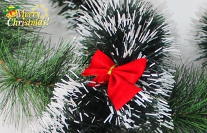 Gros plan d'une guirlande de Noël vert foncé avec pointes givrées et un nœud en tissu rouge