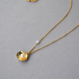 Close-up of a gold shell pendant with a white pearl on a delicate dainty chain
