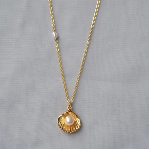 Detail of gold shell pendant necklace with white pearl on soft grey textured fabric
