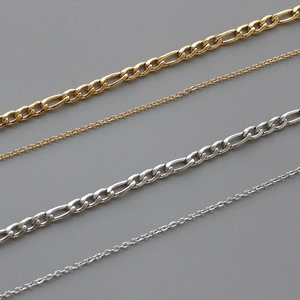 Detailed close-up of gold Figaro chains and silver link necklaces on grey background