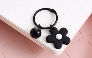 Detail of a black flower charm keychain with a bell on an open notebook page