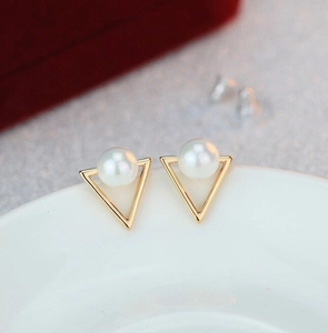 Macro shot of gold triangle pearl studs on a white plate with an elegant background
