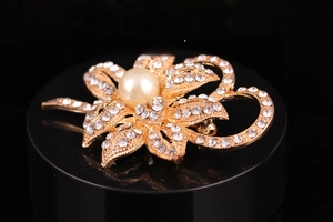 Close-up of golden floral brooch with large white pearl and sparkling rhinestones