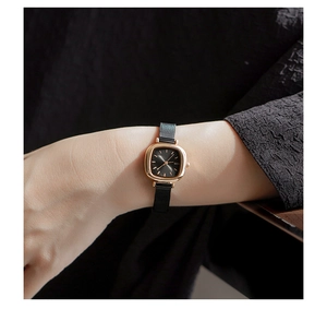Detail of square gold watch face with black mesh strap worn on a woman's wrist