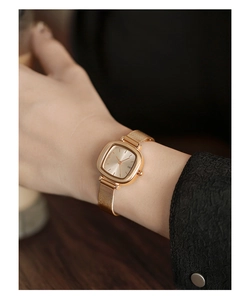 Detailed shot of a gold square watch with mesh strap on a model's wrist over wood