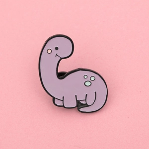 Close-up of cute purple cartoon dinosaur enamel pin with green spots and pink blush