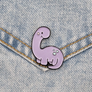 Detail of a purple cartoon dinosaur enamel pin on blue denim fabric background