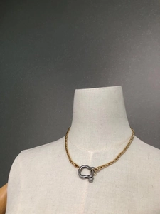 Close-up of golden wide chain necklace featuring a diamond-studded horseshoe pendant