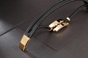 Detailed macro of black braided leather bracelet with golden razor blade metal ornament