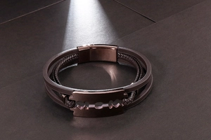 Close-up of a dark brown braided leather bracelet with a bronze razor blade pendant