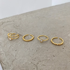 Top view of four gold-plated 925 silver rings with zircons on grey cement background