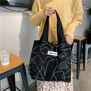 Detail of black tote bag featuring artistic white abstract lines and rectangular label