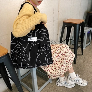 Black canvas tote bag with white abstract lines shown on model in a casual setting