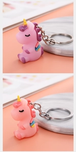 Detail of cute cartoon unicorn keychains in pink, purple, and orange colors on a marble surface