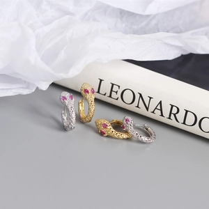 Macro view of gold and silver snake earrings featuring textured scales and red gemstones