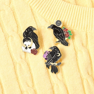 Detailed close-up of gothic raven enamel pins featuring skulls and roses on yellow knitwear