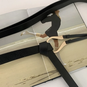Close-up of black lychee grain leather thin belt with gold streamlined horseshoe buckle