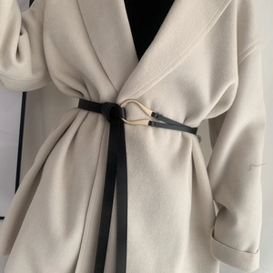 Close-up of black knot leather belt with gold horseshoe buckle on beige coat