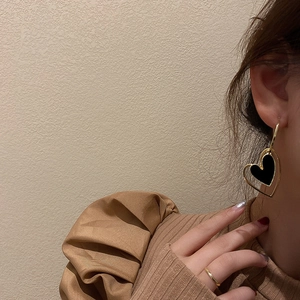 Vintage gold hollow heart earrings with black enamel inlay worn by a female model