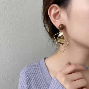 Asymmetric irregular gold and brown drip oil earrings worn by a model on white background