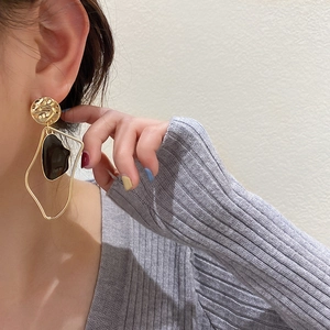 Detailed view of model wearing gold asymmetric geometric earrings with black drip oil