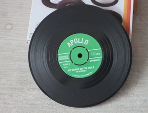 Top view of retro vinyl record coaster with green label on light wood grain table surface