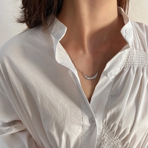 Detailed view of a silver leaf texture pendant on a slender chain worn on a white shirt