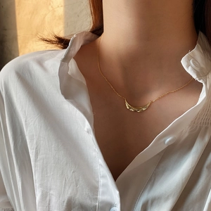 Close-up of a gold leaf textured necklace on model wearing a white shirt with warm light