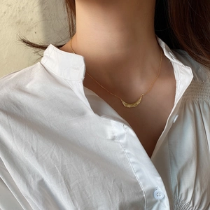 Detail of a minimalist gold branch-textured necklace worn over a white shirt