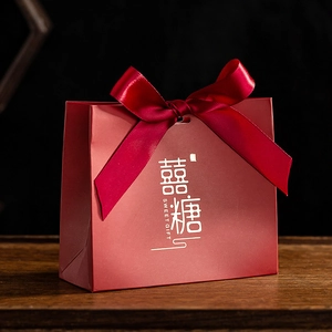 Close-up of red paper wedding candy box with gold foil lettering and matching silk ribbon