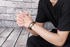 Detail of multi-layer black leather bracelet featuring a golden dog-shaped metal charm