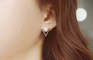Detail of silver triangular stud earring with a central pearl on a female model's ear