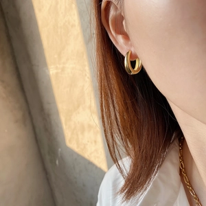 Close-up of a minimalist golden wide hoop earring worn by a model in soft natural sunlight